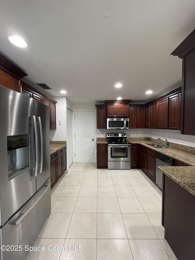 kitchen with dark stone countertops, stainless steel appliances, sink, and light tile patterned floors