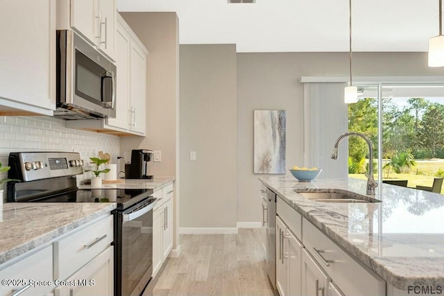 kitchen featuring light wood finished floors, stainless steel appliances, backsplash, white cabinets, and a sink