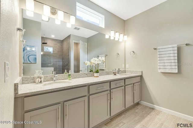 bathroom with a tile shower, wood finished floors, a sink, and baseboards