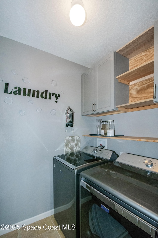 laundry area with cabinets, tile patterned floors, washing machine and dryer, and a textured ceiling