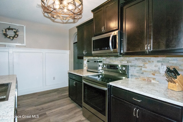 kitchen with appliances with stainless steel finishes, tasteful backsplash, wood-type flooring, a notable chandelier, and dark brown cabinetry