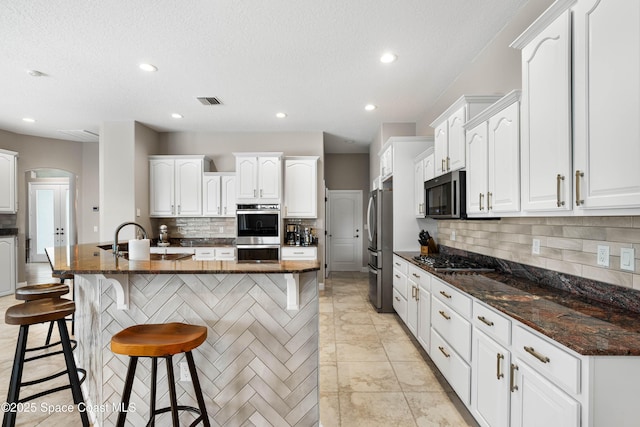 kitchen featuring stainless steel appliances, white cabinetry, and an island with sink