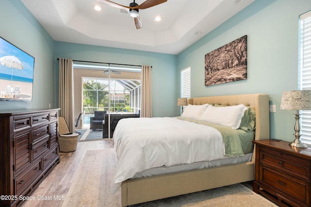 bedroom featuring ceiling fan, access to exterior, a raised ceiling, and light hardwood / wood-style floors