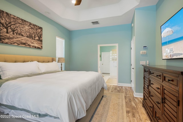 bedroom with a tray ceiling, ceiling fan, and light wood-type flooring