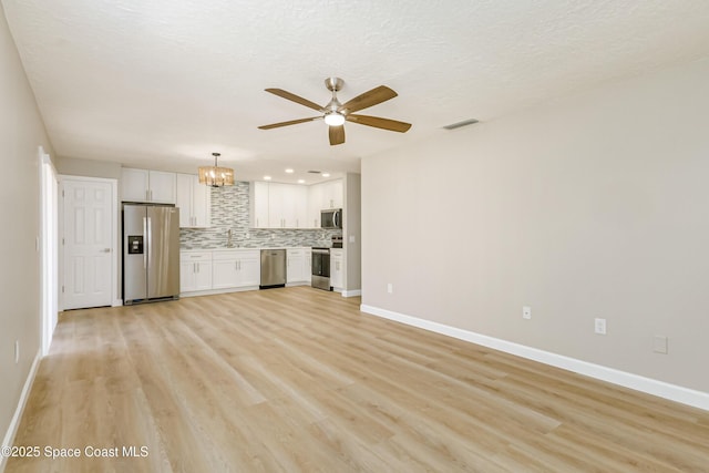 unfurnished living room with sink, ceiling fan with notable chandelier, a textured ceiling, and light wood-type flooring