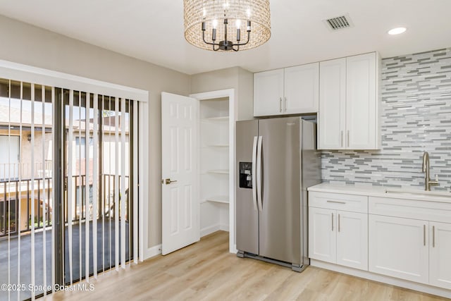 kitchen featuring sink, stainless steel fridge, light hardwood / wood-style flooring, white cabinetry, and decorative backsplash