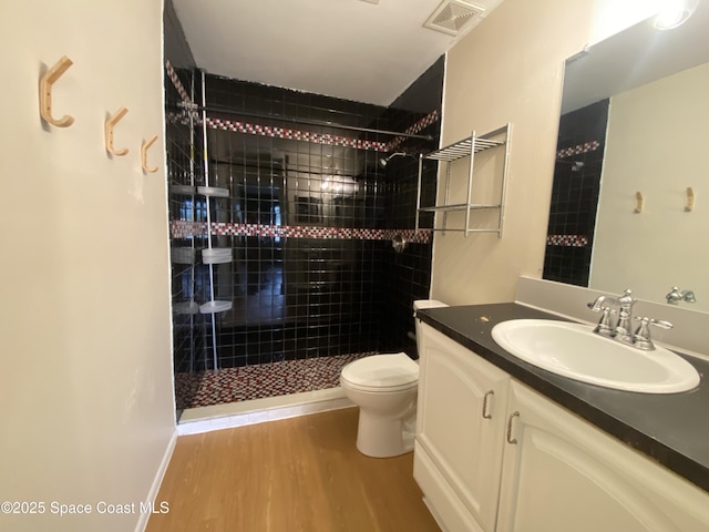 bathroom featuring hardwood / wood-style flooring, vanity, a tile shower, and toilet