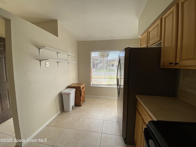 kitchen with light tile patterned flooring, vaulted ceiling, black fridge, and stove