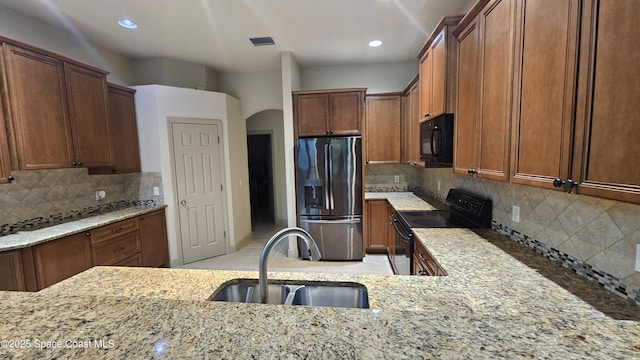 kitchen with light stone counters, sink, tasteful backsplash, and black appliances