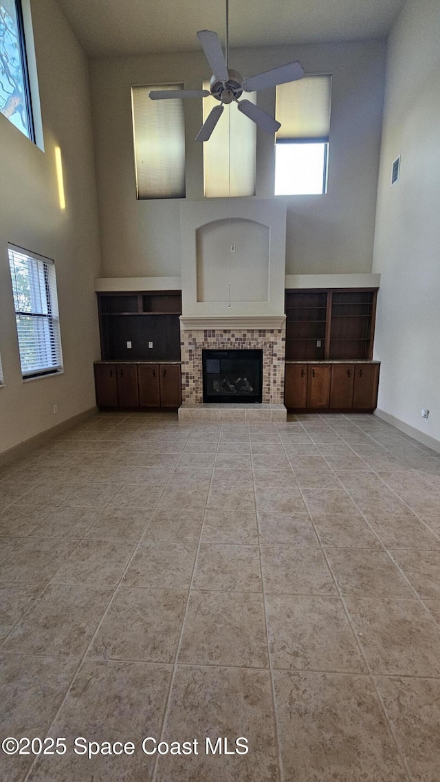 unfurnished living room with ceiling fan, a tiled fireplace, and a towering ceiling