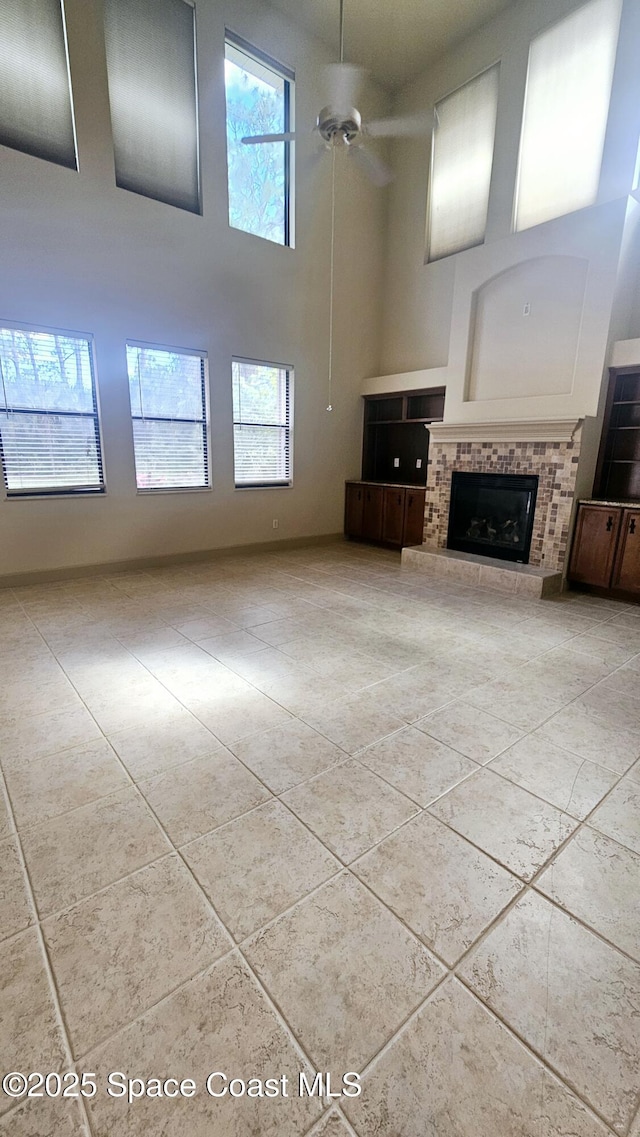 unfurnished living room with tile patterned flooring, ceiling fan, a towering ceiling, and a fireplace