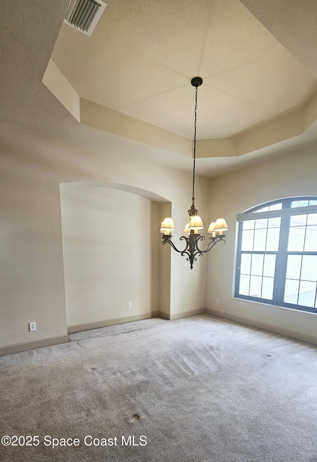 empty room featuring a notable chandelier, a raised ceiling, and carpet