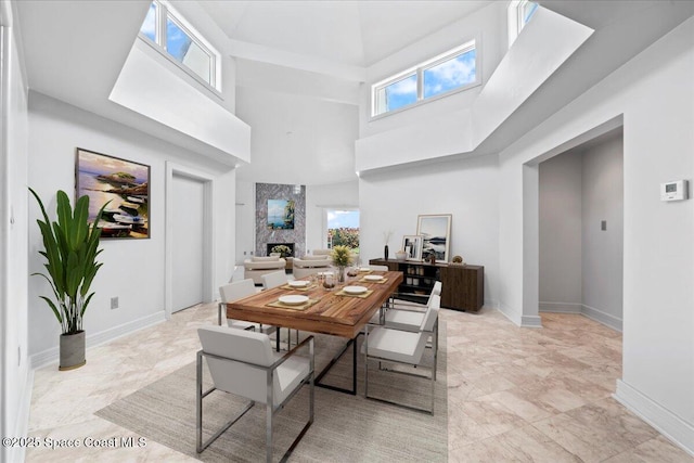 dining area featuring a large fireplace, a wealth of natural light, and a towering ceiling