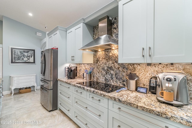 kitchen featuring white cabinetry, stainless steel fridge, light stone countertops, black electric cooktop, and wall chimney exhaust hood