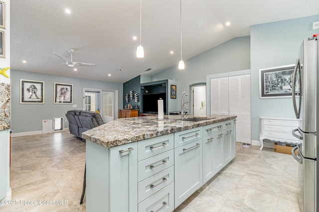 kitchen featuring decorative light fixtures, sink, stainless steel fridge, light stone countertops, and a center island with sink