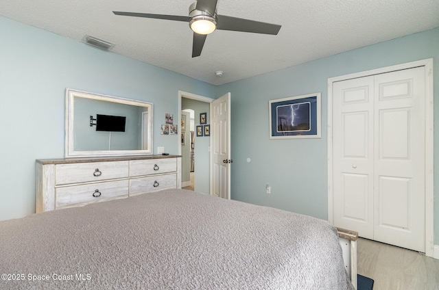 bedroom with ceiling fan, light hardwood / wood-style floors, a closet, and a textured ceiling