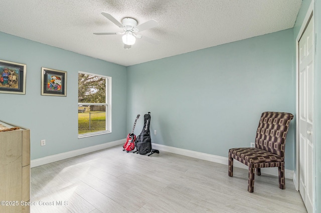 living area with ceiling fan, a textured ceiling, and light hardwood / wood-style flooring