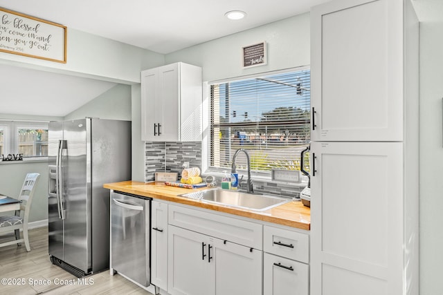 kitchen with sink, butcher block counters, stainless steel appliances, white cabinets, and decorative backsplash