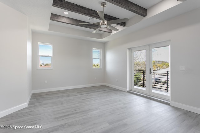 spare room featuring beamed ceiling, a healthy amount of sunlight, and light wood-type flooring