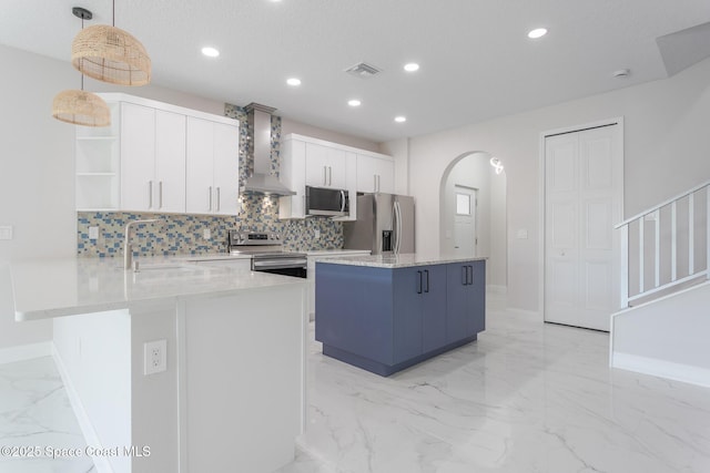 kitchen with pendant lighting, appliances with stainless steel finishes, white cabinetry, kitchen peninsula, and wall chimney exhaust hood