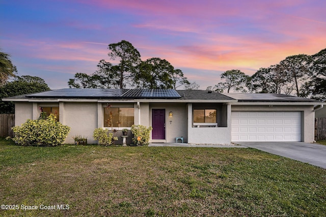 ranch-style home with a garage, a lawn, and solar panels