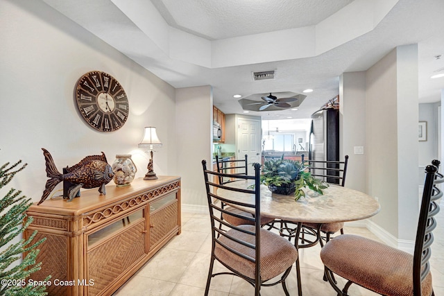 dining room with a raised ceiling, light tile patterned flooring, ceiling fan, and a textured ceiling