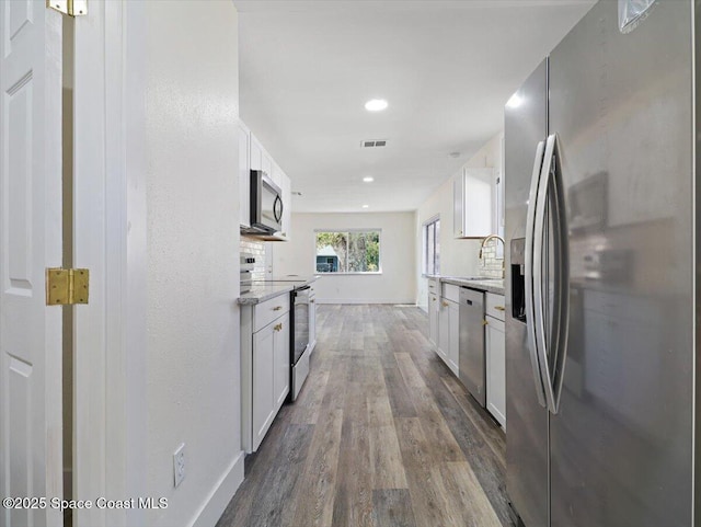 kitchen featuring appliances with stainless steel finishes, white cabinetry, light stone counters, and hardwood / wood-style flooring