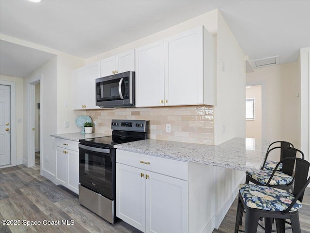 kitchen with stainless steel appliances, white cabinetry, and light stone counters