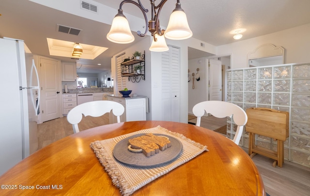 dining area with crown molding, a tray ceiling, and light hardwood / wood-style floors