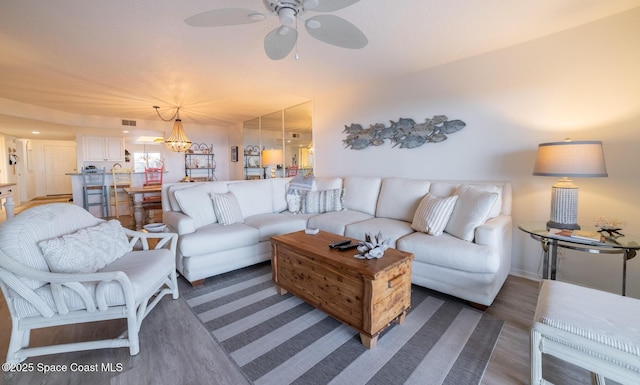 living room featuring ceiling fan with notable chandelier and dark wood-type flooring