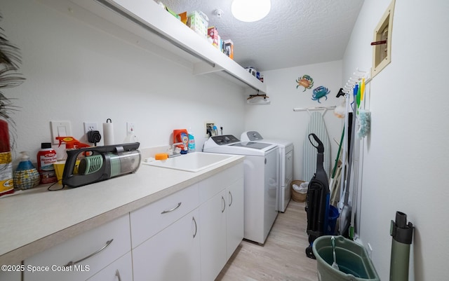 laundry room featuring sink, cabinets, light hardwood / wood-style flooring, washer and dryer, and a textured ceiling