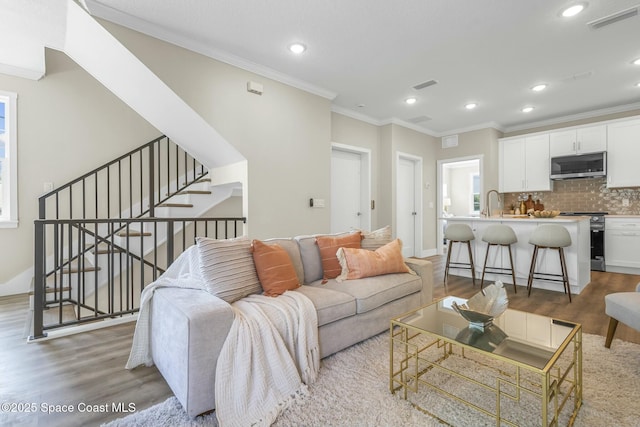 living room featuring crown molding, sink, and hardwood / wood-style floors