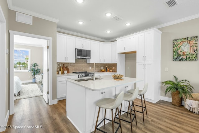 kitchen featuring crown molding, a kitchen island with sink, hardwood / wood-style floors, tasteful backsplash, and white cabinets