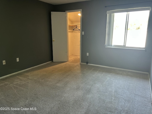 unfurnished bedroom with a spacious closet, a closet, baseboards, and carpet floors