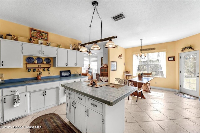 kitchen with white cabinets, hanging light fixtures, a center island, light tile patterned floors, and a textured ceiling