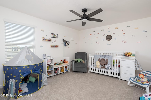 bedroom featuring a crib, light colored carpet, and ceiling fan