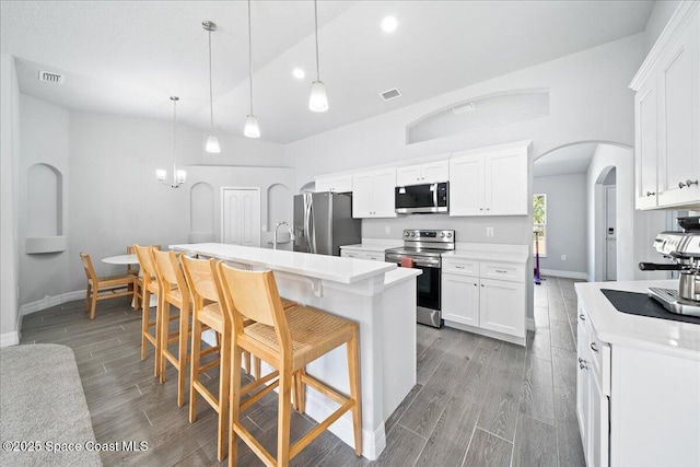 kitchen with stainless steel appliances, decorative light fixtures, a center island with sink, and white cabinets