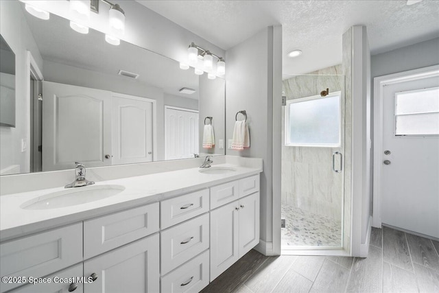 bathroom with vanity, a shower with shower door, and a textured ceiling