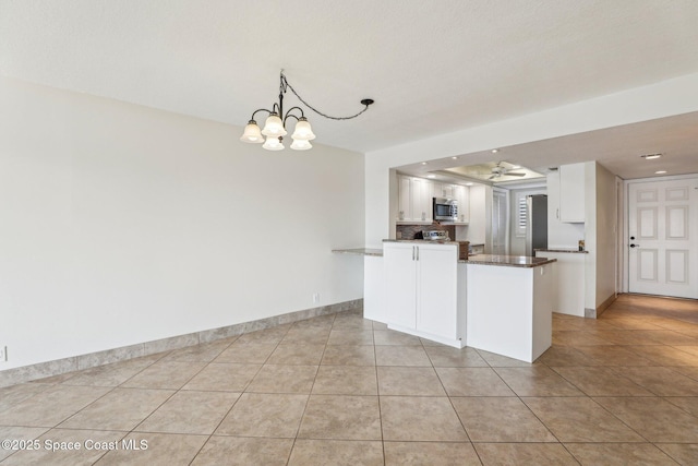 kitchen with light tile patterned flooring, decorative light fixtures, kitchen peninsula, stainless steel appliances, and white cabinets