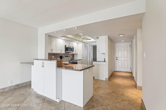 kitchen featuring dark stone counters, appliances with stainless steel finishes, light tile patterned flooring, white cabinets, and decorative backsplash