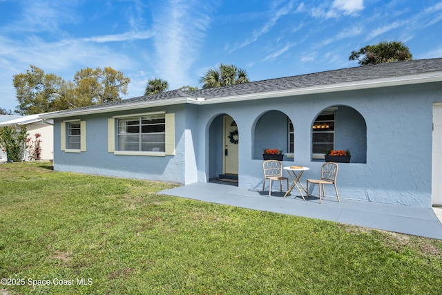 rear view of property featuring a shingled roof, a lawn, and stucco siding