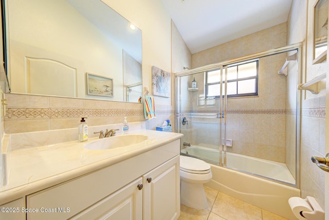 full bathroom with shower / bath combination with glass door, tile patterned flooring, tile walls, vanity, and toilet