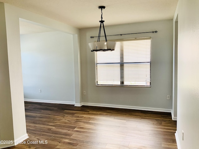 unfurnished dining area with a notable chandelier, wood finished floors, and baseboards