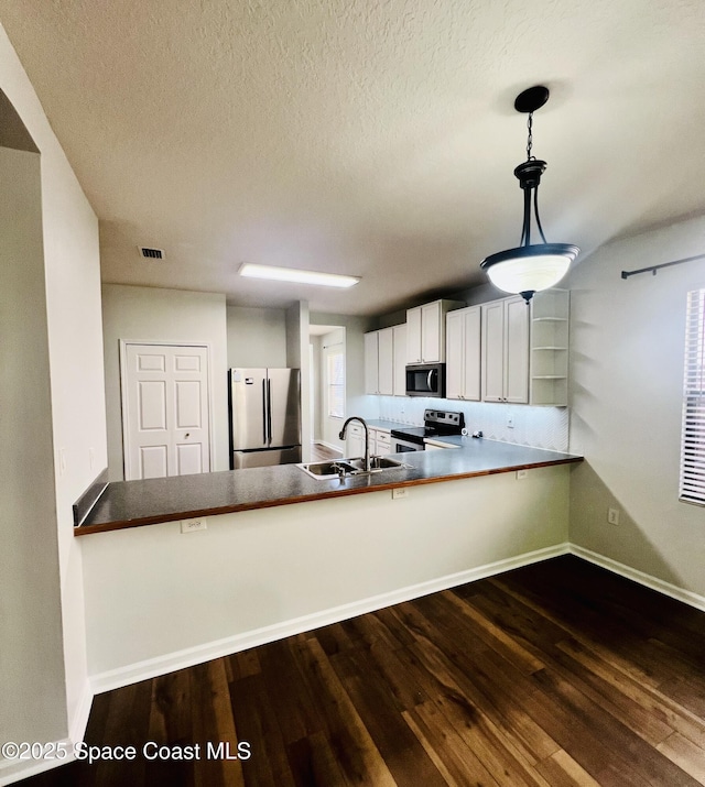 kitchen featuring a sink, stainless steel appliances, dark wood-type flooring, and a peninsula