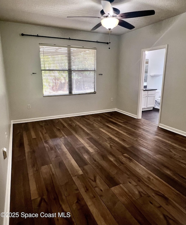 empty room with dark wood finished floors, a ceiling fan, baseboards, and a textured ceiling