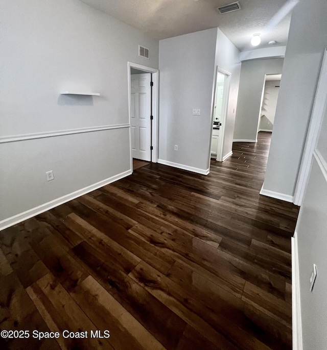 unfurnished room featuring visible vents, dark wood-type flooring, and baseboards