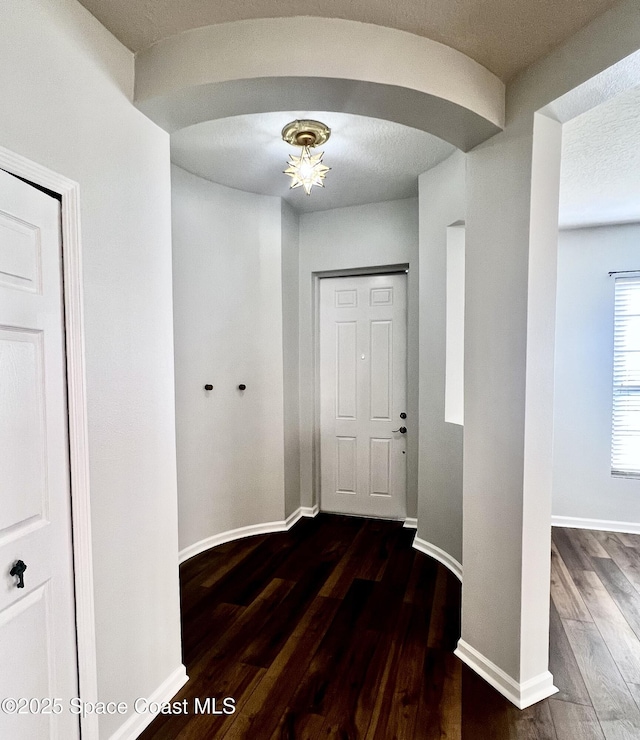 interior space with dark wood-type flooring, arched walkways, baseboards, and a textured ceiling