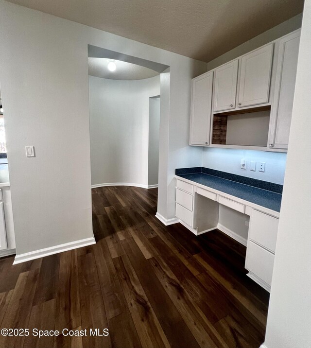 kitchen with white cabinets, built in study area, dark wood-type flooring, and baseboards