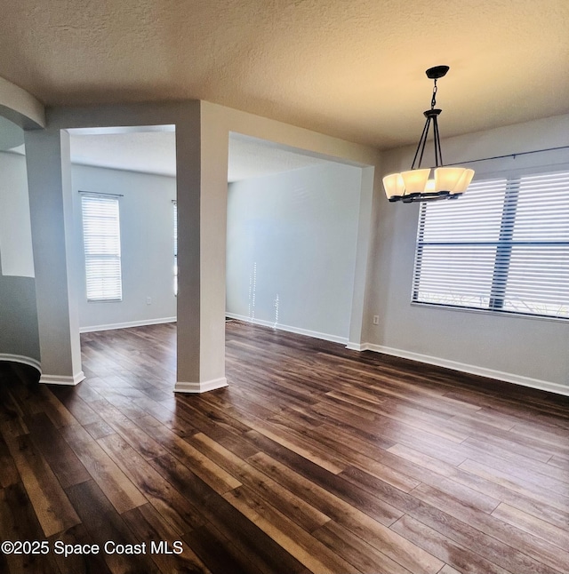 unfurnished dining area featuring baseboards, a textured ceiling, and dark wood finished floors