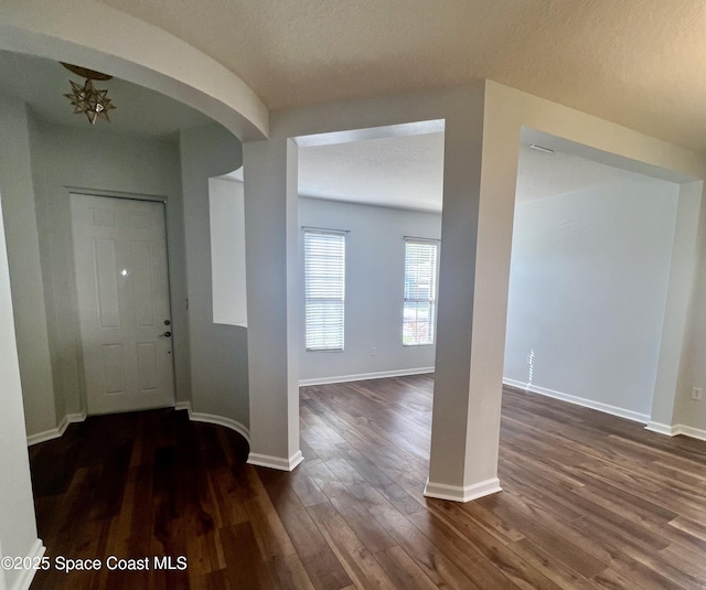 foyer entrance with arched walkways, a textured ceiling, dark wood-type flooring, and baseboards